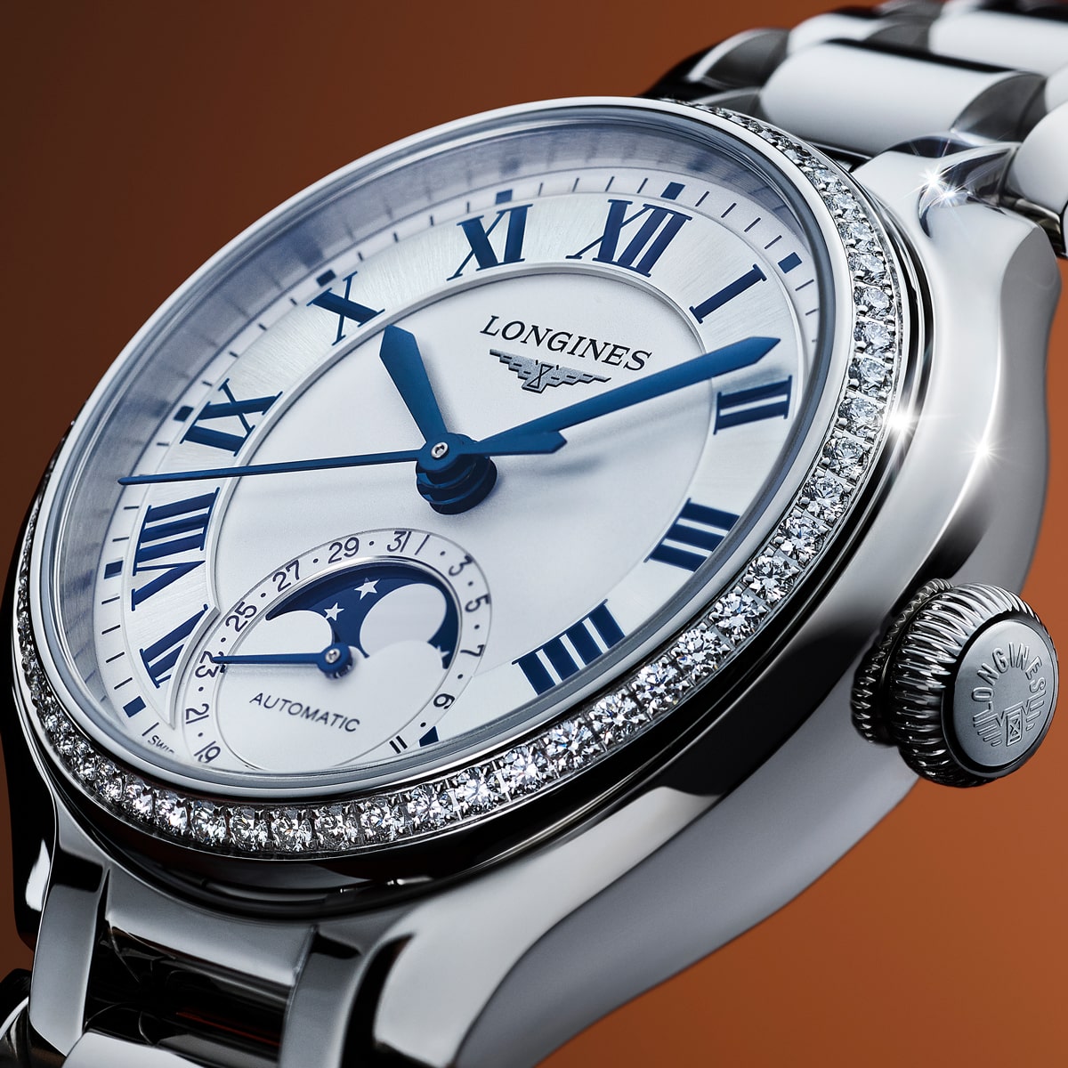 Eine Nahaufnahme einer luxuriösen Longines-Armbanduhr mit silbernem Band, blauen römischen Ziffern, Mondphasenanzeige und diamantbesetzter Lünette vor einem warmen Hintergrund mit Farbverlauf.